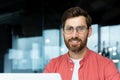 Close-up portrait of mature businessman inside office, man with beard and red shirt smiling and looking at camera Royalty Free Stock Photo