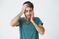 Close up portrait of mature caucasian bearded man in blue t-shirt, holding hand on forehead and cheek looking tired and