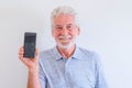 Close up and portrait of mature man holding a phone and showing at the camera it - online and social network senior lifestyle and Royalty Free Stock Photo