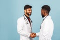 Close-up portrait of a medical worker in a white lab coat with a stethoscope conferring with a young doctor on a blue background