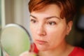 Close up portrait of Middle age woman holding round mirror and carefully looking at her reflection