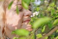 Close-up portrait of middle-aged blonde woman, woman sniffing white flowers of blooming apple tree from a tree branch Royalty Free Stock Photo