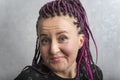 Close up portrait of middle-aged woman with pink dreadlocks writhing grimace. Emotion of surprise and smirk