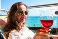 Portrait of modern long hair woman holding in hand a glass of red wine on the background seascape view.