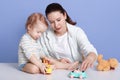 Close up portrait of mother and baby boy having fun with toys, sitting isolated over blue background, infant wearing stripped Royalty Free Stock Photo