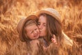 Close-up portrait of mother and daughter in straw hat in wheat field. Young woman kisses little girl Royalty Free Stock Photo