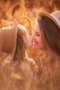 Close-up portrait of mother and daughter in straw hat in wheat field. Little girl kisses young woman Royalty Free Stock Photo