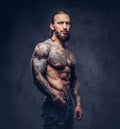 Close-up portrait of a muscular naked bearded tattoed male with a stylish haircut, isolated on a dark background.