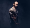 Close-up portrait of a muscular naked bearded tattoed male with a stylish haircut, isolated on a dark background.