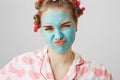 Close-up portrait of nasty meany girl in facial mask and hair-curlers, wearing pyjamas and squinting while looking at Royalty Free Stock Photo