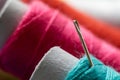 A close up portrait of a needle stuck in a roll of sewing thread. In the background there are other spools of yarn in different Royalty Free Stock Photo