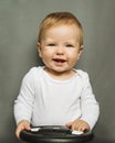 Close-up portrait of a nine-month-old baby girl with blond hair and blue eyes, dressed in a white bodysuit on a gray background