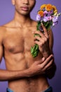 Close-up portrait of nude torso of boy with flowers in hand. Sensual latino young man posing