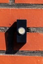 A close up portrait of an old black doorbell with a white button on a red brick wall, ready to be pressed to ring the bell and Royalty Free Stock Photo