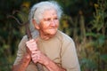 Close-up portrait of an old woman with gray hair holding a rusty pitchfork or chopper in her hands, face in deep wrinkles,