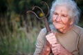 Close-up portrait of an old woman with gray hair holding a rusty pitchfork or chopper in her hands, face in deep wrinkles,