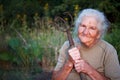 Close-up portrait of an old woman with gray hair holding a rusty pitchfork or chopper in her hands, face in deep wrinkles,