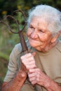 Close-up portrait of an old woman with gray hair holding a rusty pitchfork or chopper in her hands, face in deep wrinkles,