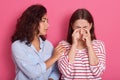 Close up portrait of one teenage girl comforting another after break up, female wearing striped shirt crying in studio, her friend