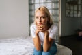 Close-up portrait of pensive young blonde woman sitting alone in living room and sad looking at camera holding hands on Royalty Free Stock Photo