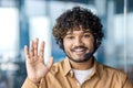 Close-up portrait photo of a smiling young Indian man wearing a headset working in the office, greeting and waving at Royalty Free Stock Photo