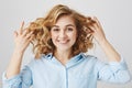 Close-up portrait of playful attractive woman with frizzle hairstyle holding her curly hair and smiling joyfully at