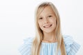 Close-up portrait of pleased adorable blond girl in blue blouse, smiling cheerfully and gazing at camera, being polite