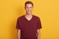 Close up portrait of pleased young guy dressed maroon casual t shirt, looking smiling at camera, expresses happyness, model posing