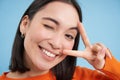 Close up portrait of positive asian woman, winks and shows peave, v-sign gesture, sticks tongue and smiles, stands over Royalty Free Stock Photo