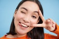 Close up portrait of positive asian woman, winks and shows peave, v-sign gesture, sticks tongue and smiles, stands over Royalty Free Stock Photo