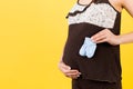 Close up portrait of pregnant woman in brown pajamas holding blue socks for a baby boy at yellow background. Future child Royalty Free Stock Photo