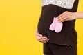 Close up portrait of pregnant woman in brown pajamas holding pink socks for a baby girl at yellow background. Waiting for a child Royalty Free Stock Photo