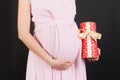 Close up portrait of pregnant woman in pink dress holding a gift box at black background. Pregnancy celebration. Copy space Royalty Free Stock Photo