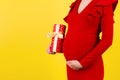 Close up portrait of pregnant woman in red dress holding a gift box at yellow background. Pregnancy celebration. Copy space Royalty Free Stock Photo