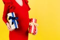 Close up portrait of pregnant woman in red dress holding two gift boxes at yellow background. Waiting for a baby boy or a baby Royalty Free Stock Photo
