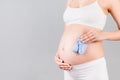 Close up portrait of pregnant woman in white underwear holding blue socks for a baby boy at gray background. Future child Royalty Free Stock Photo