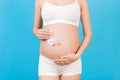 Close up portrait of pregnant woman in white underwear holding pink socks for a baby girl at blue background. Waiting for a child Royalty Free Stock Photo