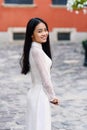 Close up portrait of pretty asian girl dressed in Ao Dai white dress on the background of red building. Royalty Free Stock Photo