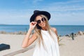 Close-up portrait of pretty blond girl with long hair is standing on the beach near sea. She wears black hat, white Royalty Free Stock Photo