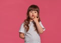 Close-up portrait of a little brunette girl dressed in a white t-shirt posing against a pink studio background. Sincere Royalty Free Stock Photo