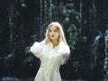 Close up portrait of pretty Caucasian woman near waterfall. Beautiful female with long blond hair wearing white dress. Background Royalty Free Stock Photo