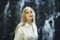 Close up portrait of pretty Caucasian woman near waterfall. Female with long blond hair wearing white dress. Water splash. Copy Royalty Free Stock Photo