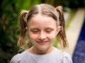 Close up portrait of pretty little girl. Face with closed eyes. Caucasian girl with two ponytails. Green tropical leaves and Royalty Free Stock Photo