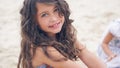 Close-up portrait of a pretty little Hispanic girl with waving in the wind long hair sitting on the beach. Royalty Free Stock Photo