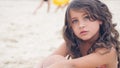 Close-up portrait of a pretty little Hispanic girl with waving in the wind long hair sitting on the beach. Royalty Free Stock Photo