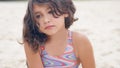 Close-up portrait of a pretty little Hispanic girl with waving in the wind long hair sitting on the beach. Royalty Free Stock Photo