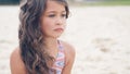 Close-up portrait of a pretty little Hispanic girl with waving in the wind long hair sitting on the beach. Royalty Free Stock Photo