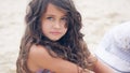 Close-up portrait of a pretty little Hispanic girl with waving in the wind long hair sitting on the beach. Royalty Free Stock Photo