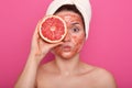 Close up portrait of pretty woman with perfect skin,posing with facial mask, holding half of grapefruit in front of her eye, lady