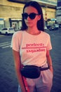 Portrait of a girl in dark sunglasses posing near a city mall. Dressed in white t-shirt, blue trousers, black waist bag Royalty Free Stock Photo